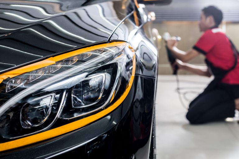 auto detailer man using tool to polish back of shiny black car